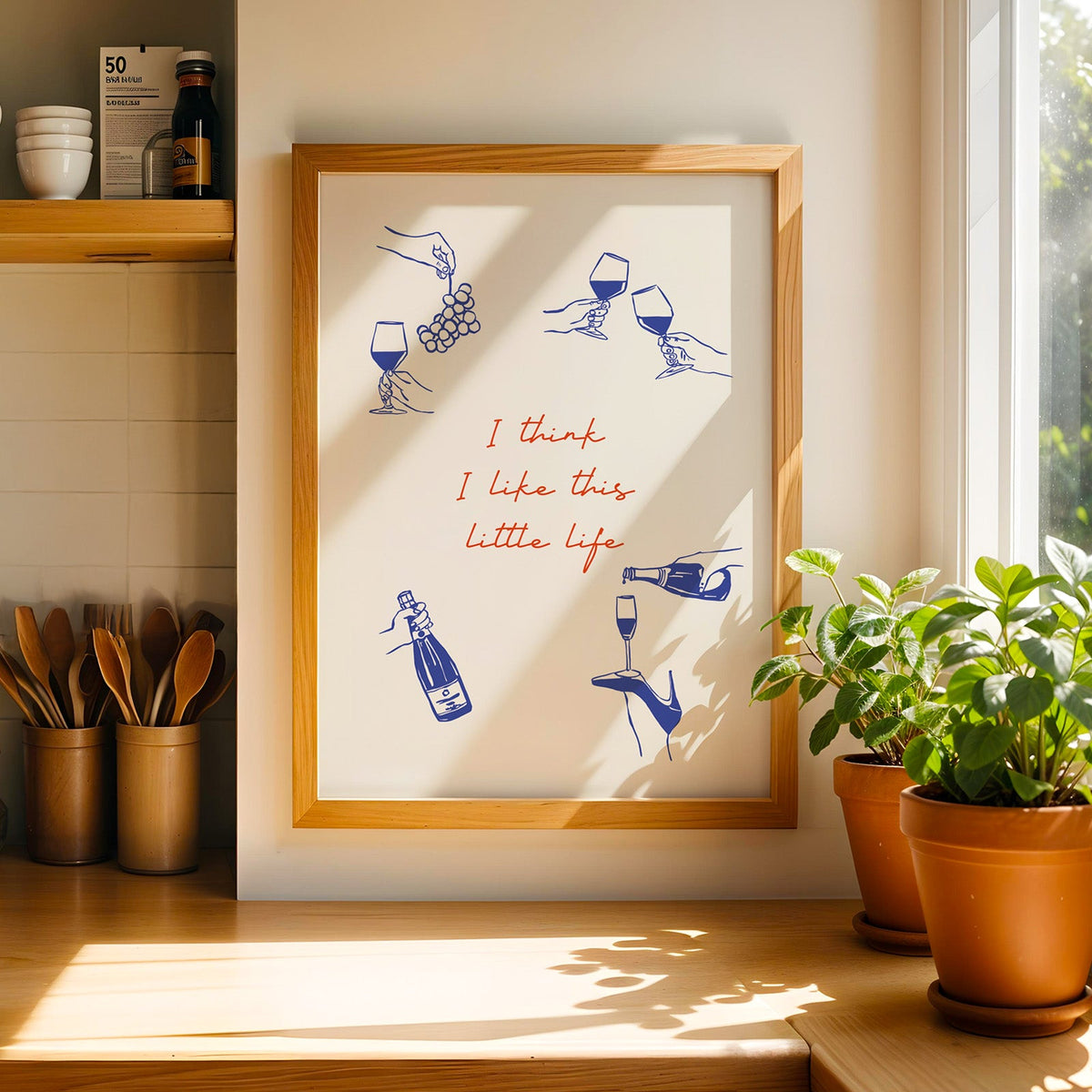 This Little Life wine print in a light pine frame beside a jar of wooden spoons
