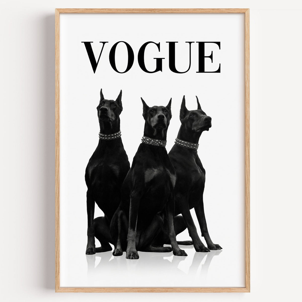 Three black Dobermans in spiked collars print in a light oak frame on a plain white wall