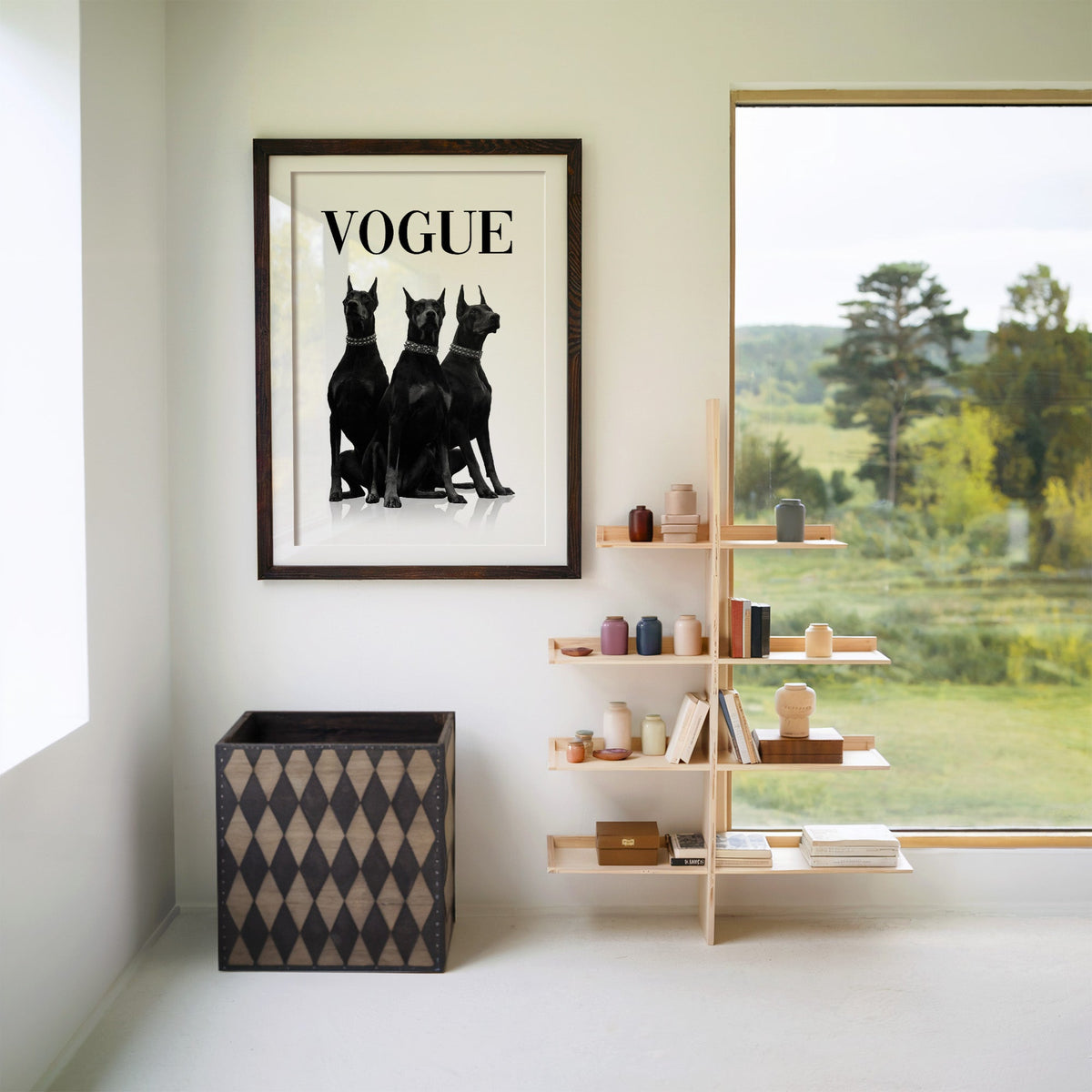 Three black Dobermans in spiked collars print in a walnut frame with a white mat beside wooden shelves and a garden window