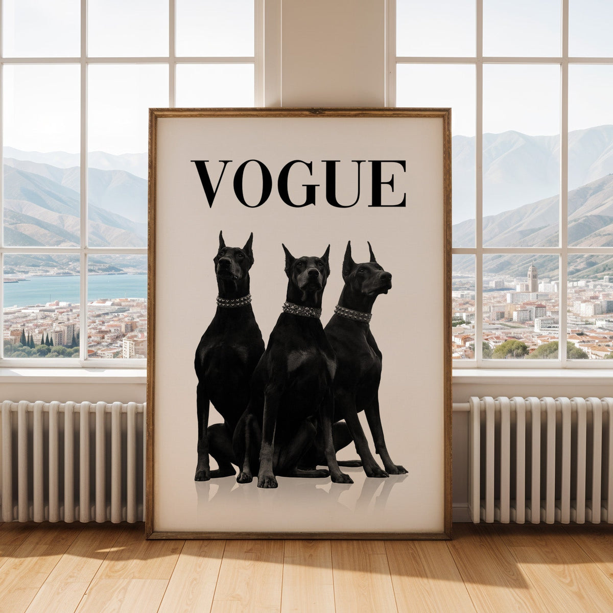 Three black Dobermans in spiked collars print shown in an antique gold frame by tall windows with a sea view