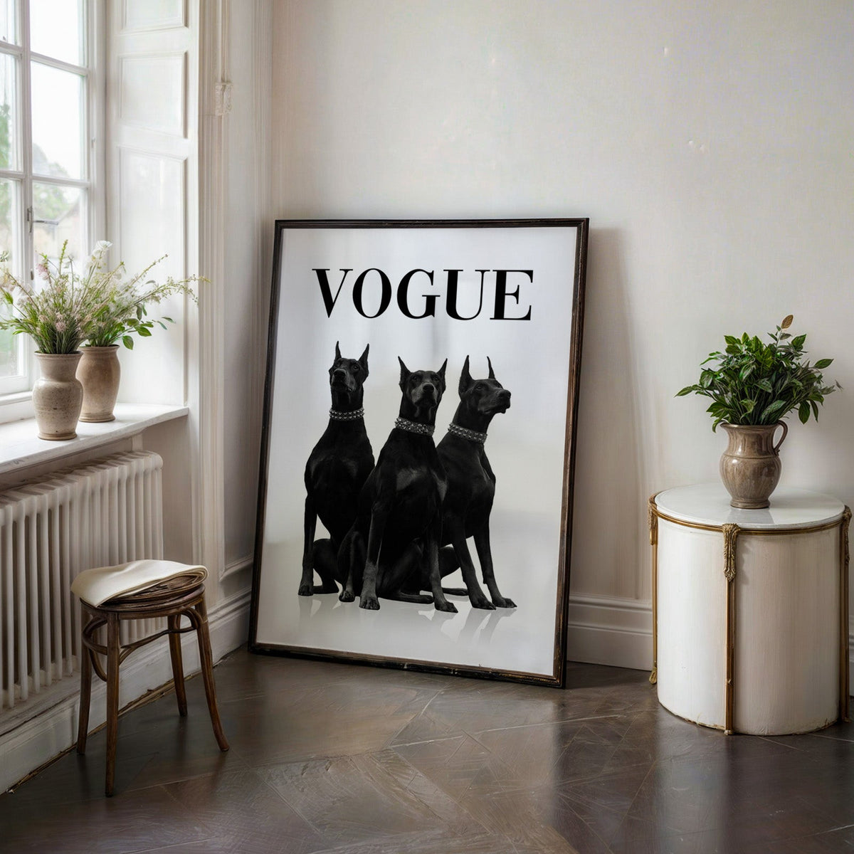 Three black Dobermans in spiked collars print in a black frame on a dark stone floor beside a white side table