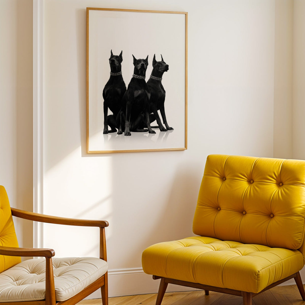 Three Dobermans in spiked collars on white print shown in a gold frame above a mustard yellow tufted armchair