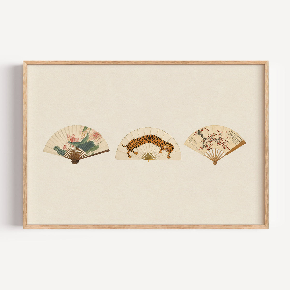 Three painted folding fans print in a light oak frame on a plain white wall
