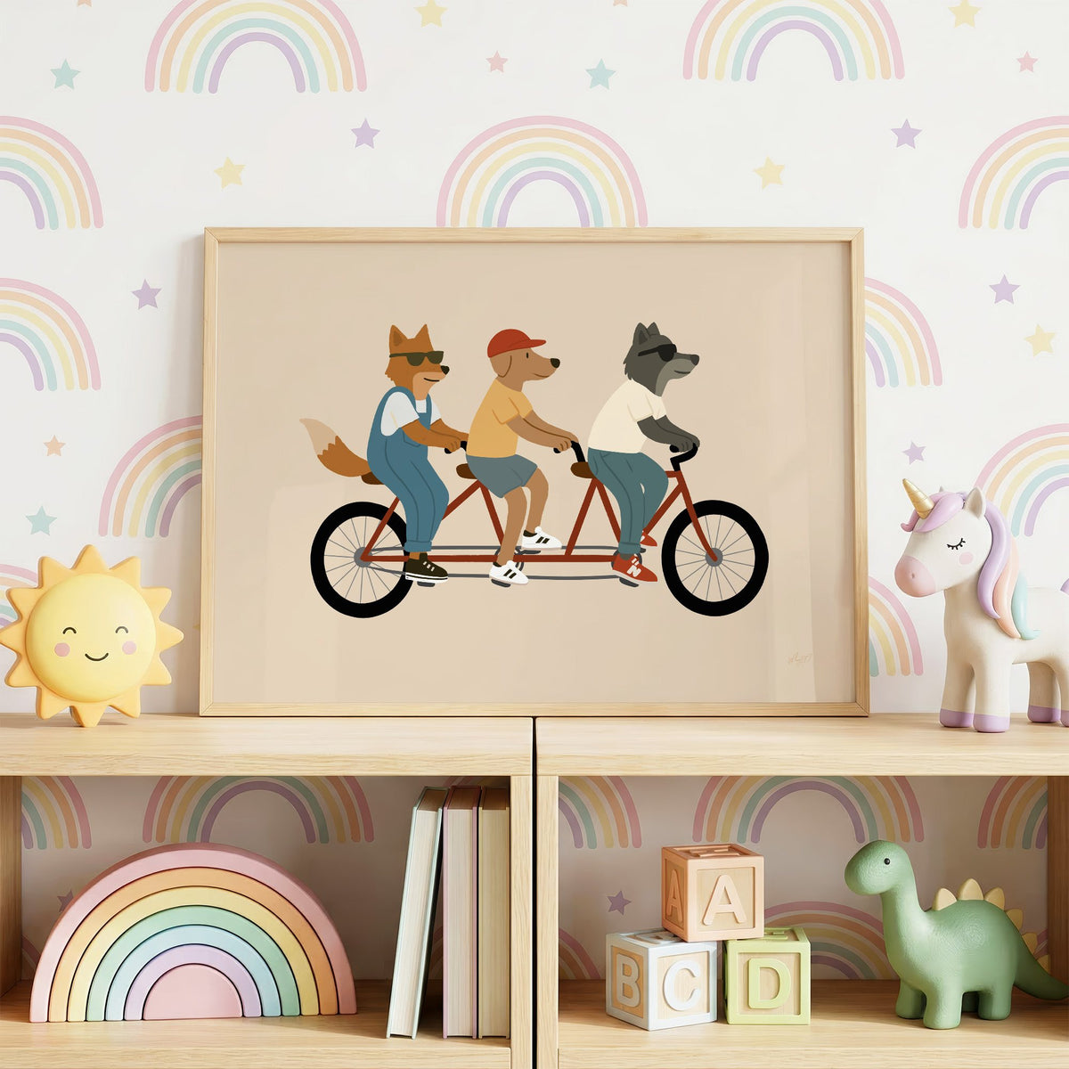 Animal friends riding tandem bike nursery print in an oak frame on a toy shelf against rainbow wallpaper