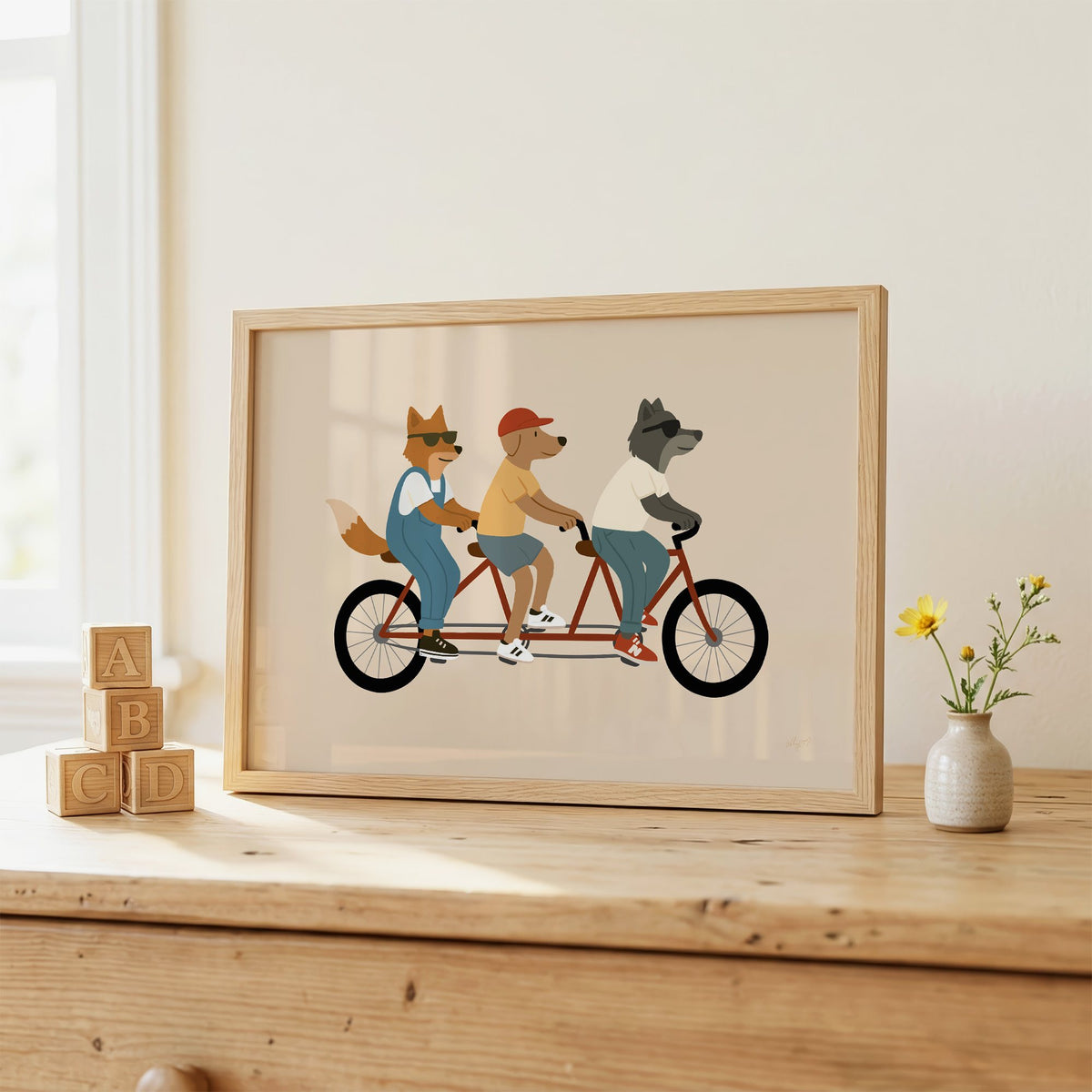 Animal friends riding tandem bike nursery print in an oak frame on a wooden dresser beside ABC blocks
