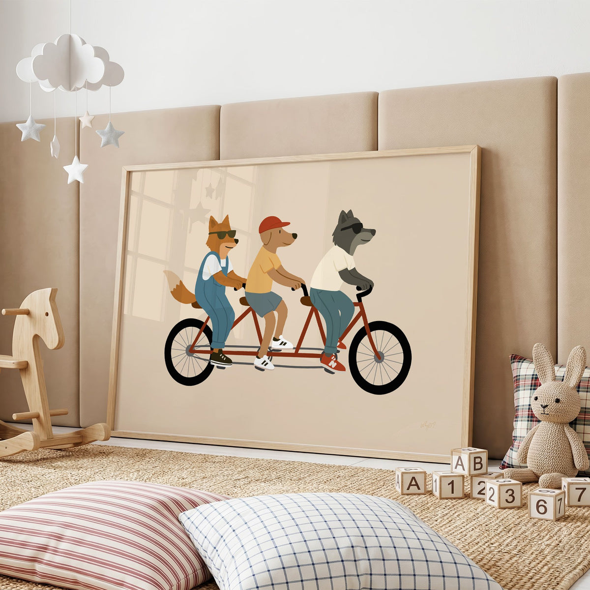 Animal friends riding tandem bike nursery print in an oak frame on a padded wall by a wooden rocking horse