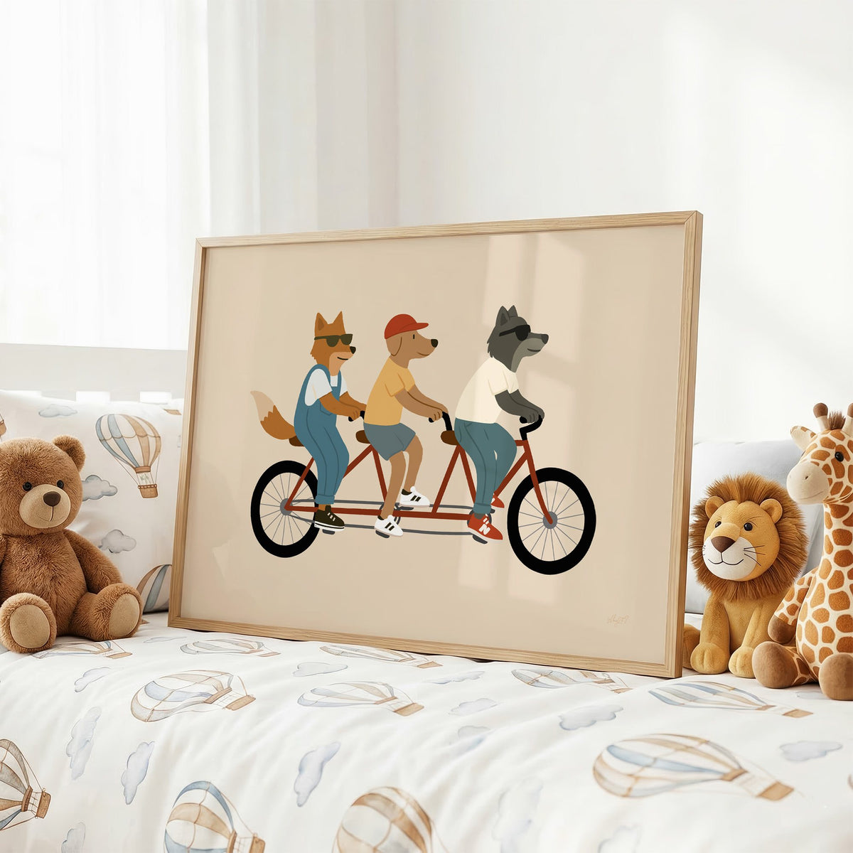 Animal friends riding tandem bike nursery print in an oak frame on a kids bed with hot air balloon bedding