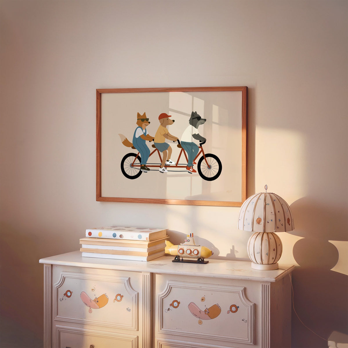 Animal friends riding tandem bike nursery print in a cherry wood frame above a painted dresser and lamp