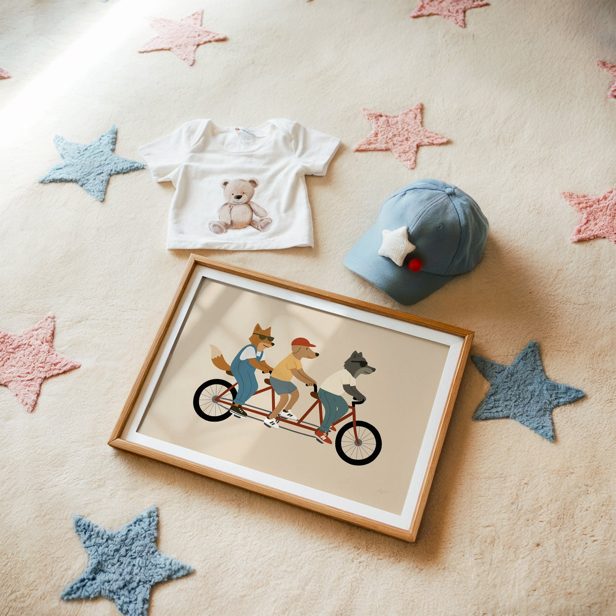 Animal friends riding tandem bike nursery print in a matted oak frame on a star rug with a baby tee