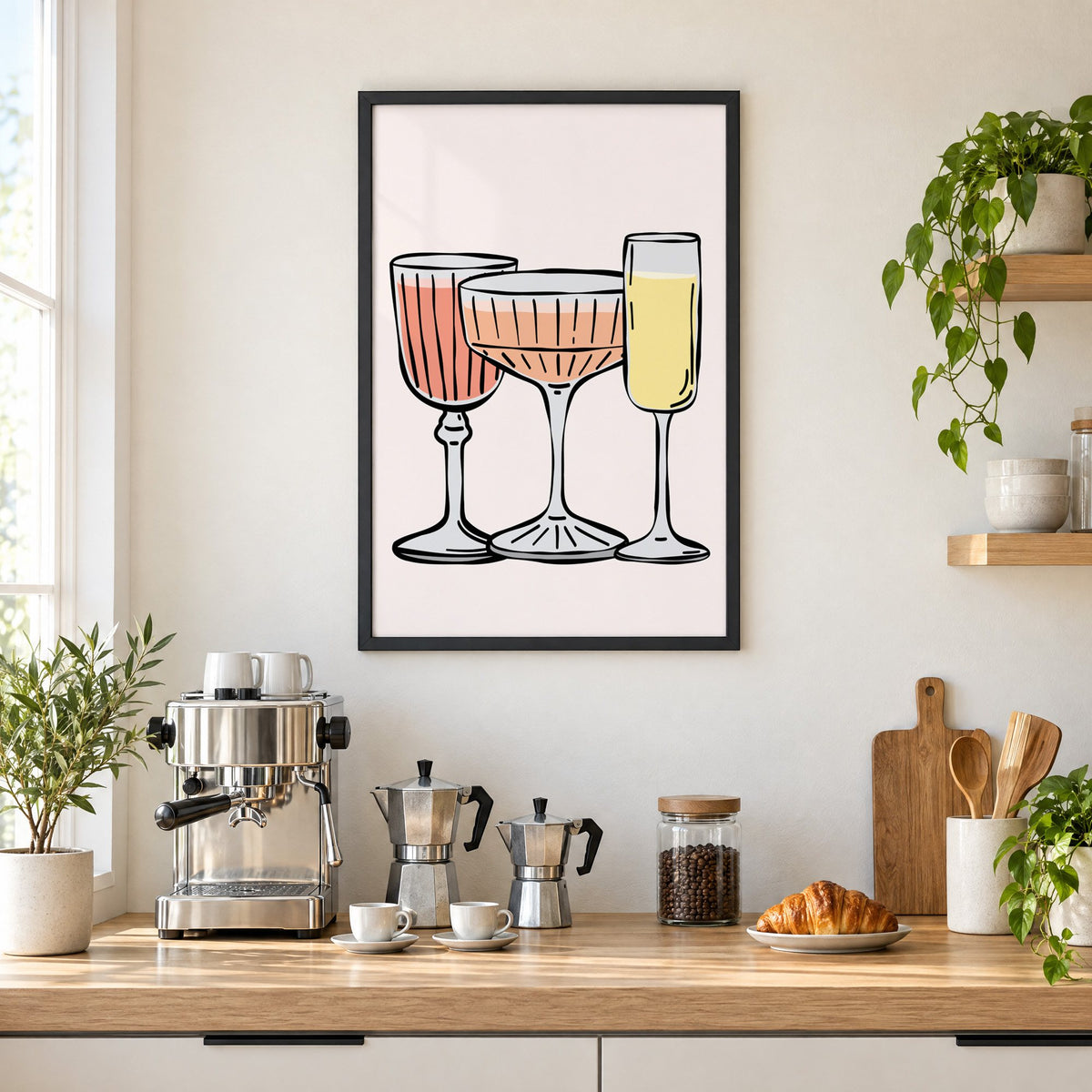 Three pastel cocktail glasses and champagne flute print in a black frame above a home espresso bar with moka pots and espresso cups