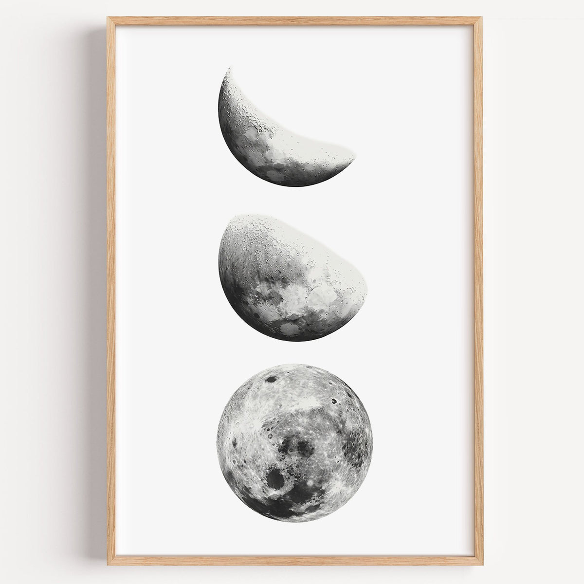 Three moon phases stacked vertically on white print in a light oak frame on a plain white wall