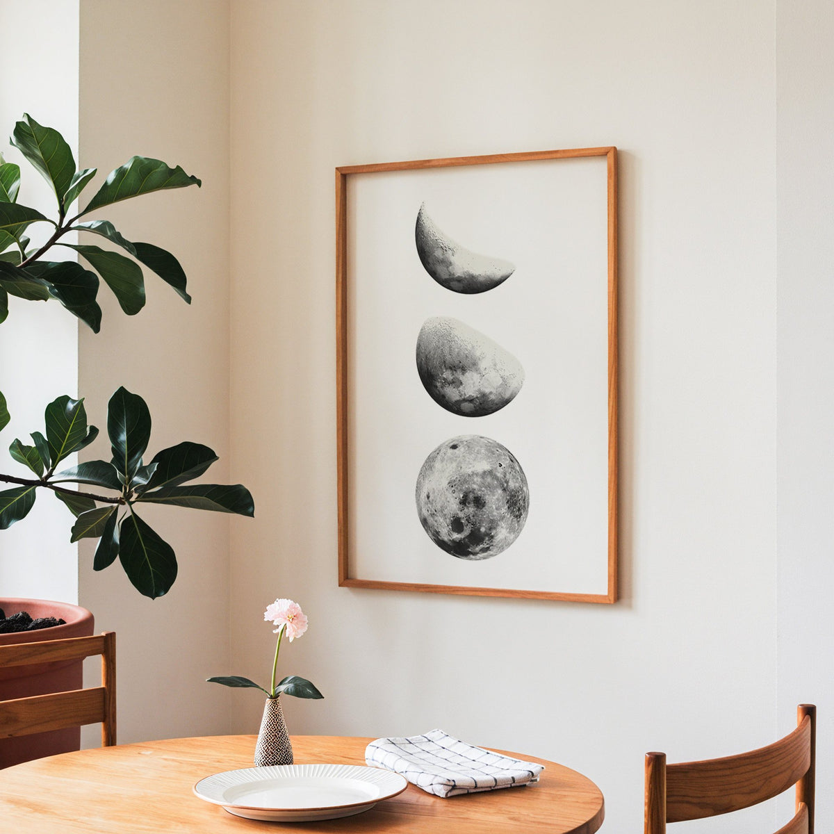 Three moon phases stacked vertically on white print in a teak frame above a round wooden dining table