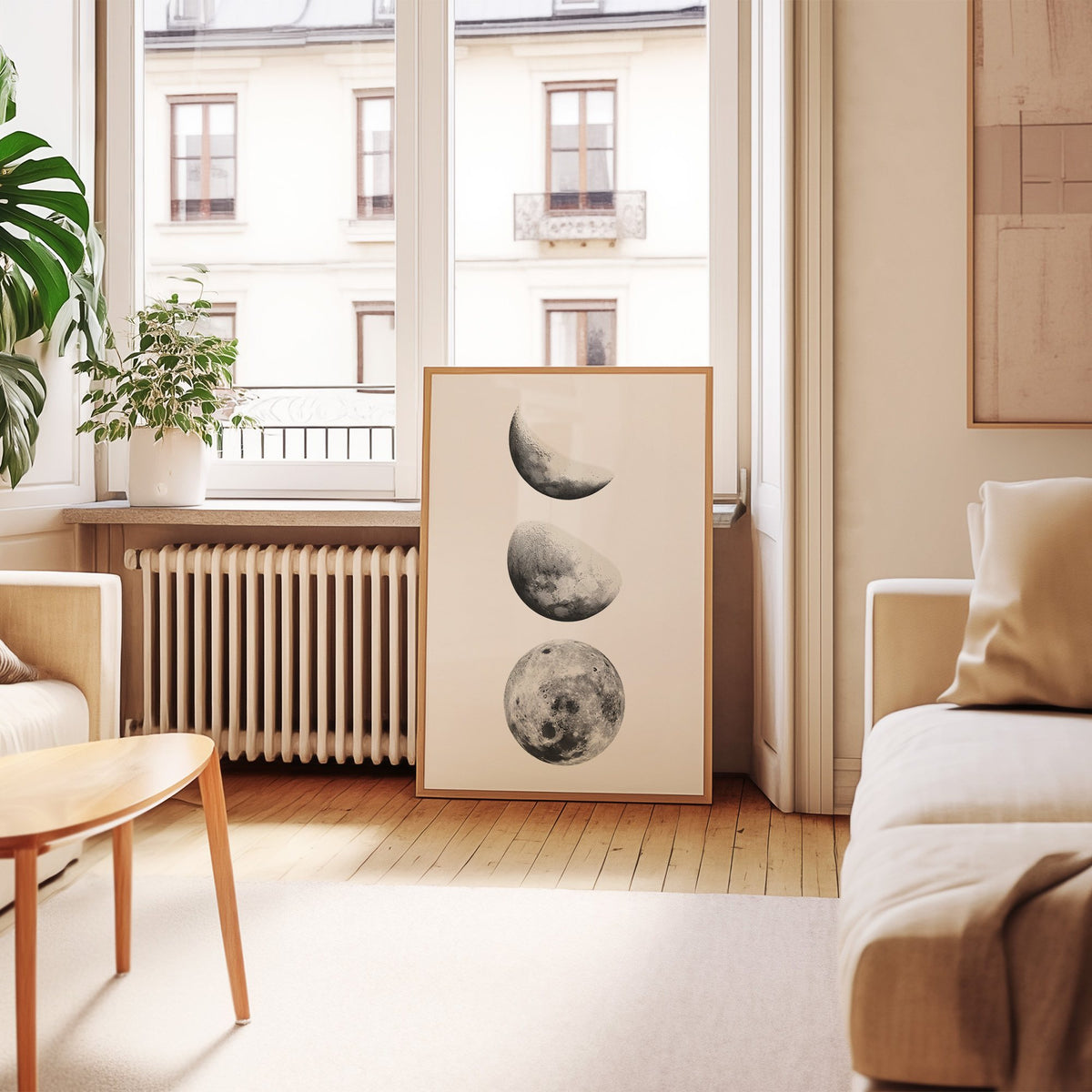 Three moon phases stacked vertically on white print in an oak frame leaning by a French window in a living room