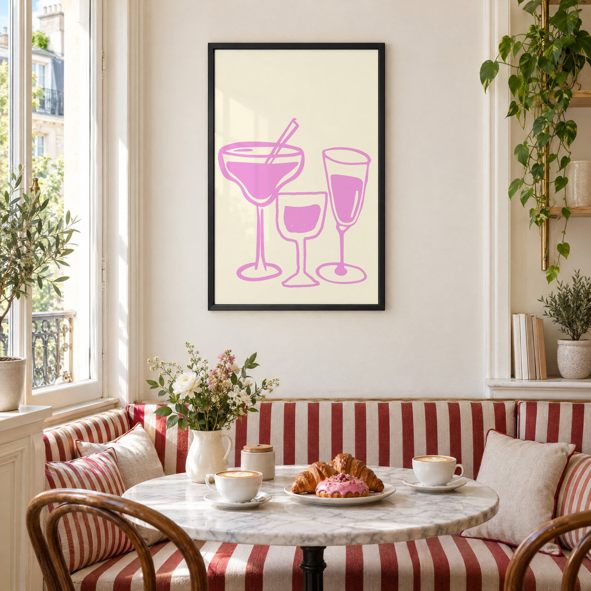 Three pink cocktail glasses linocut-style print in a black frame above a striped cafe breakfast nook with cappuccino and pastries