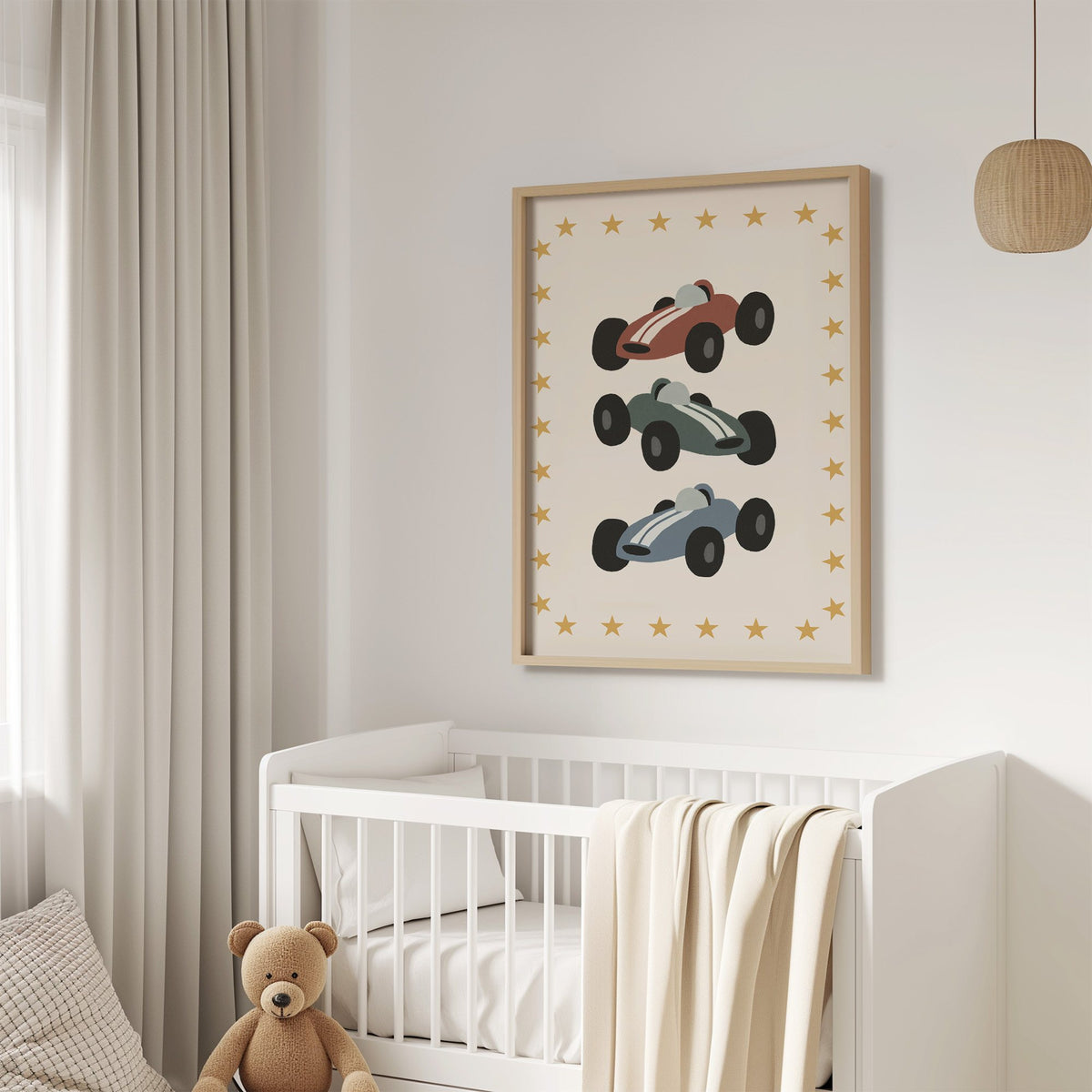 Three race cars star border nursery print in an oak frame above a white crib with a teddy bear