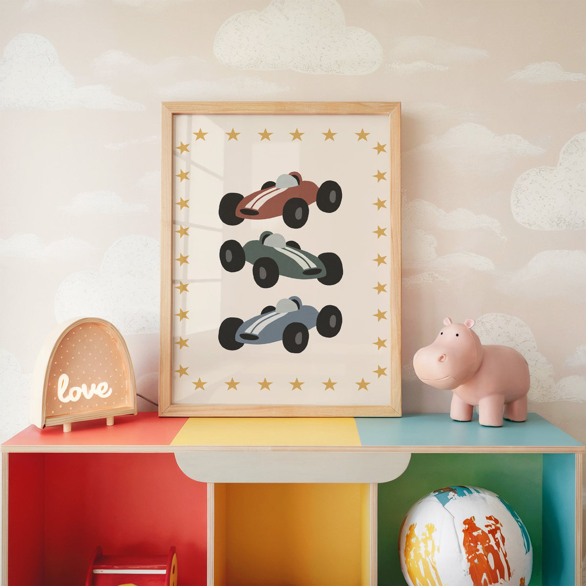 Three race cars star border nursery print in an oak frame on a rainbow toy shelf against cloud wallpaper