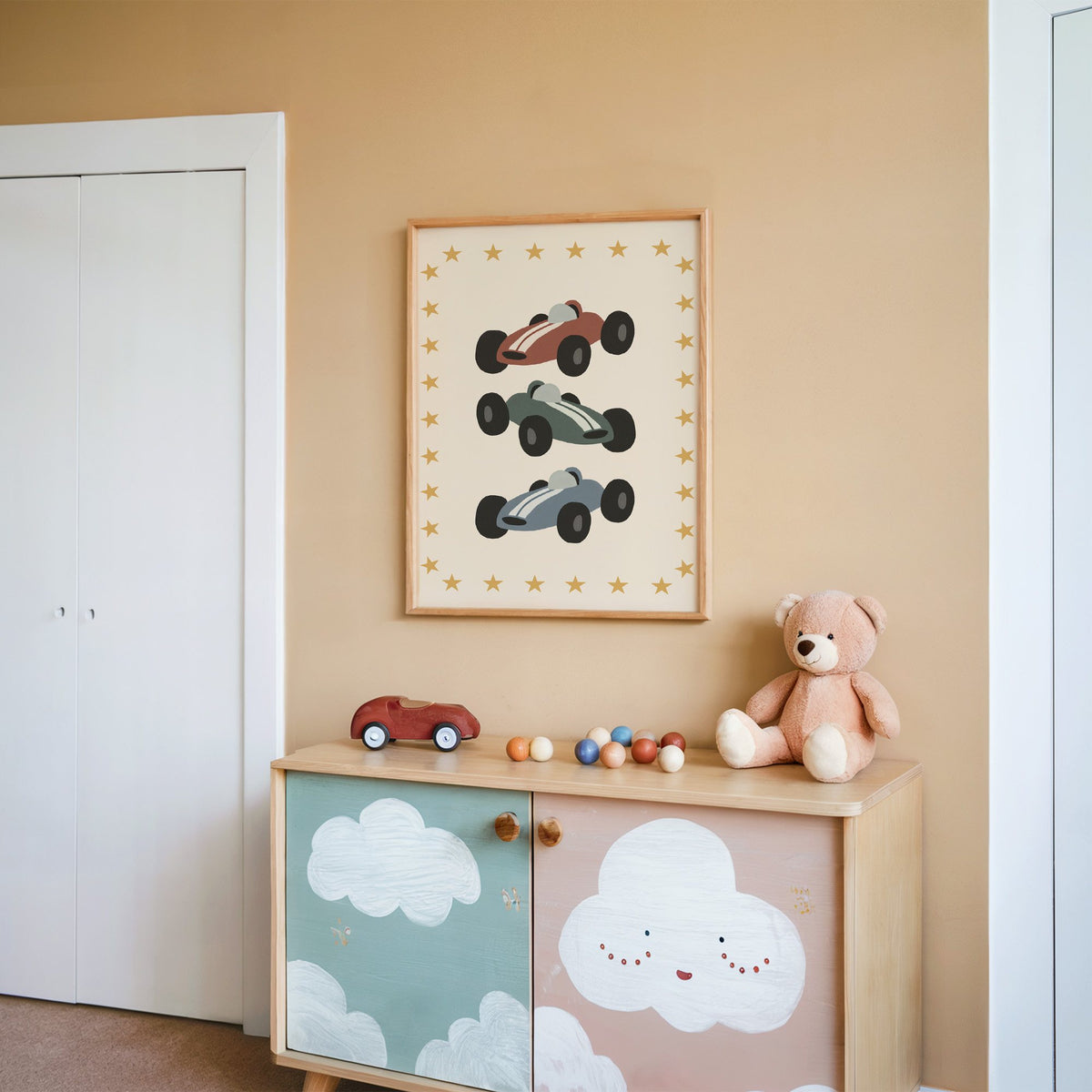 Three race cars star border nursery print in an oak frame on a peach wall above a cloud-painted cabinet