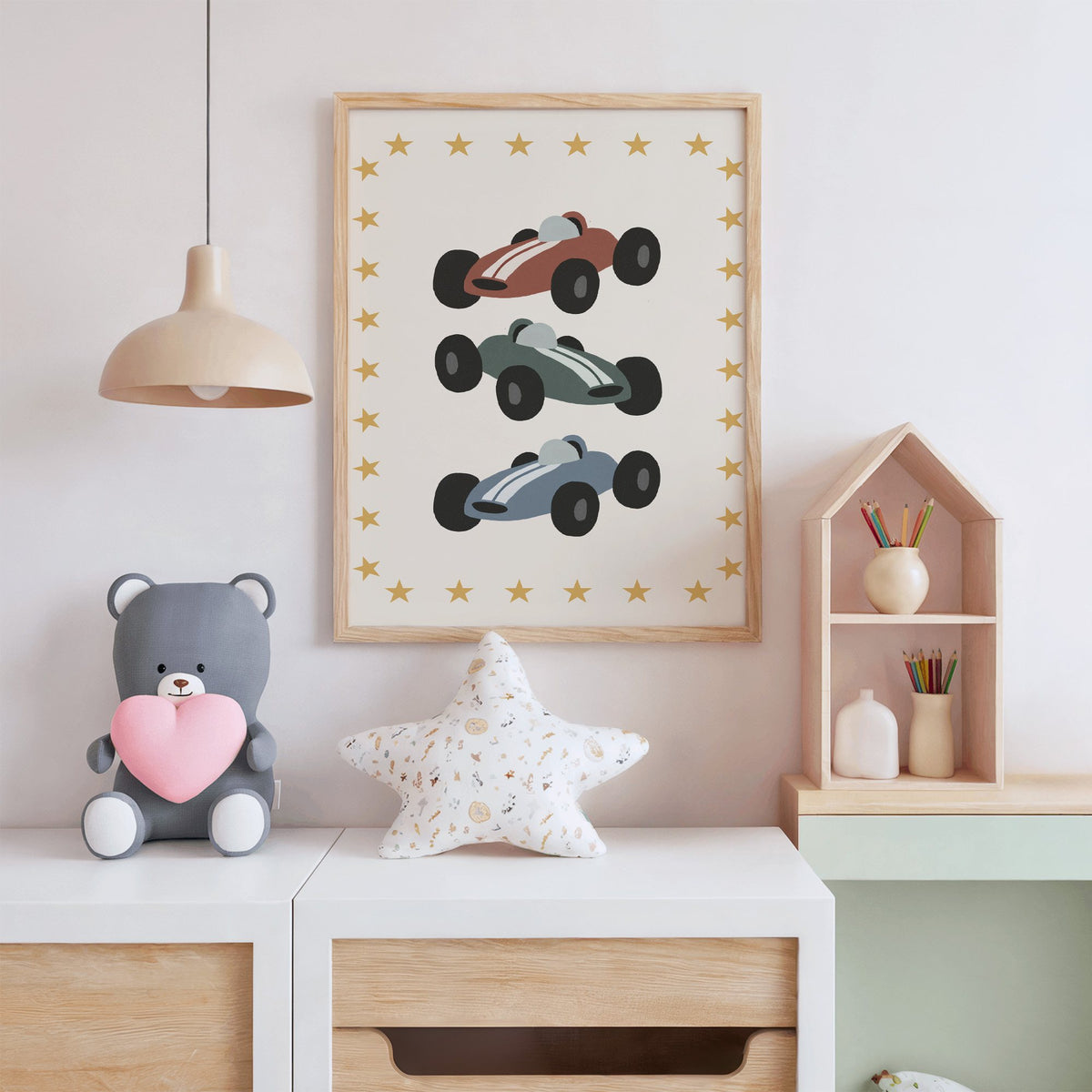 Three race cars star border nursery print in an oak frame above a white dresser with a star pillow and house shelf