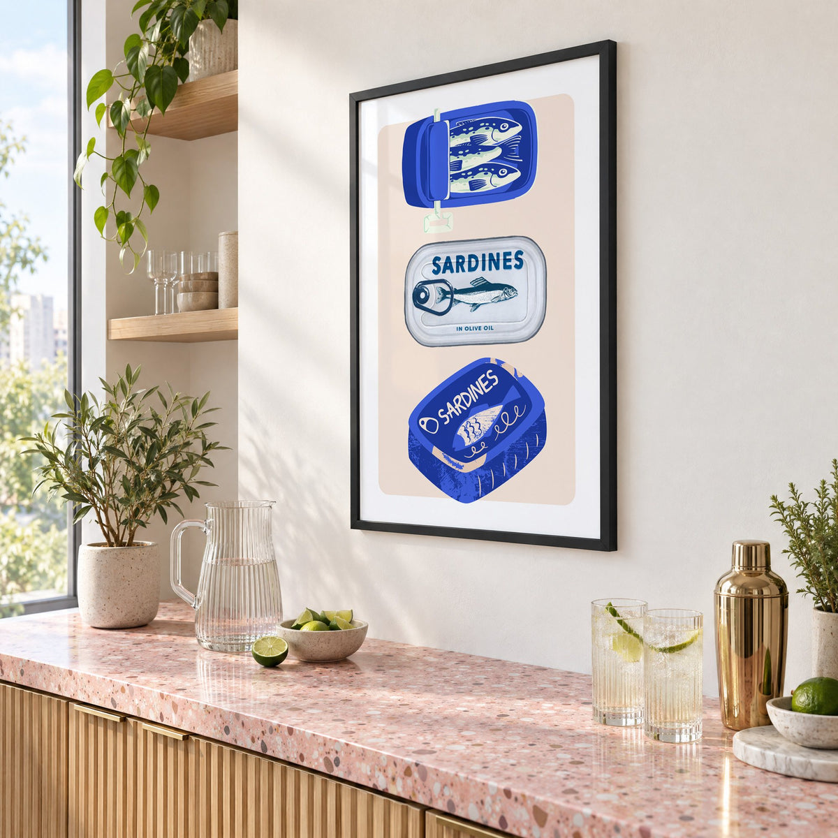 Three sardine tins cobalt print in a black frame above a pink terrazzo cocktail counter with limes, seen at an angle