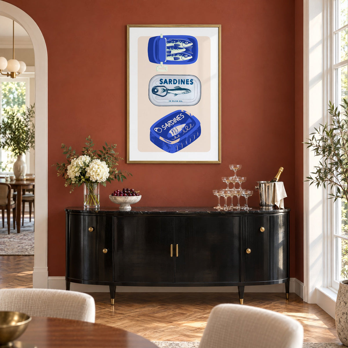 Three sardine tins cobalt print in a brass frame on a terracotta wall above a black buffet with a champagne tower