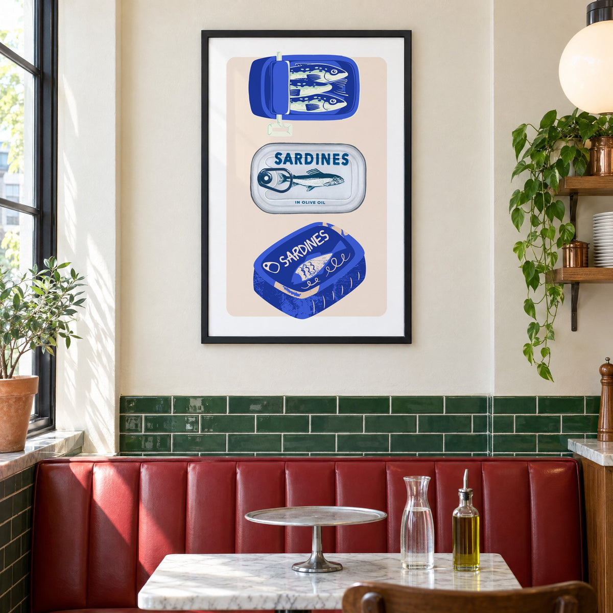 Three sardine tins cobalt print in a black frame above a red leather booth in a sunny pizzeria