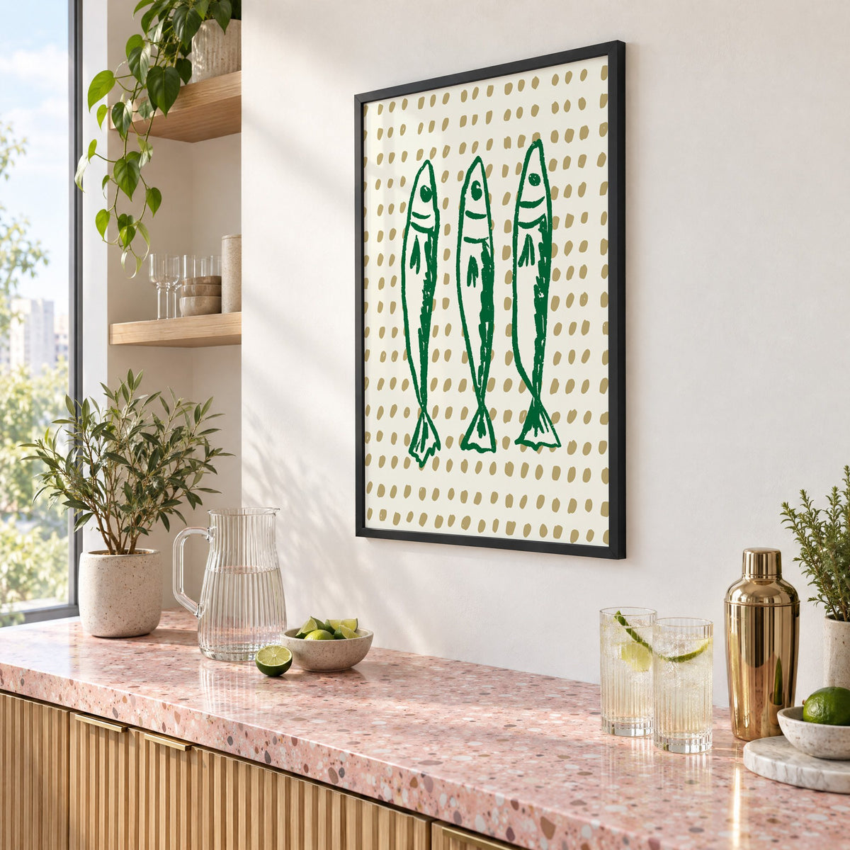 Three green sardines on dotted print in a black frame above a pink terrazzo cocktail counter with limes, seen at an angle