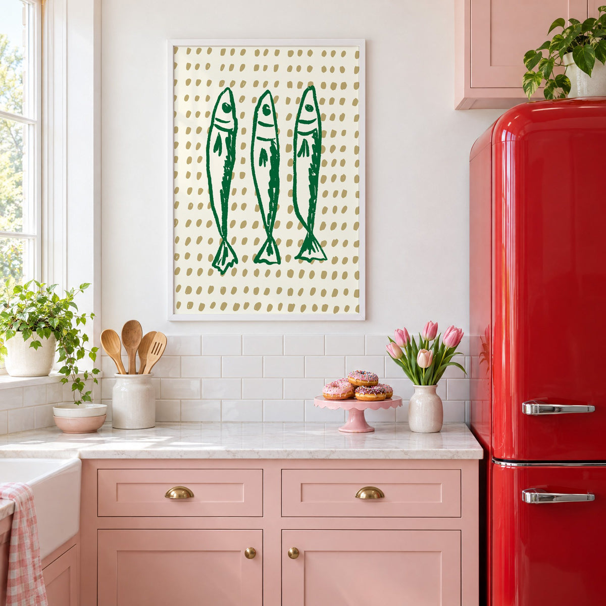 Three green sardines on dotted print in a white frame above pink cabinets beside a red retro fridge