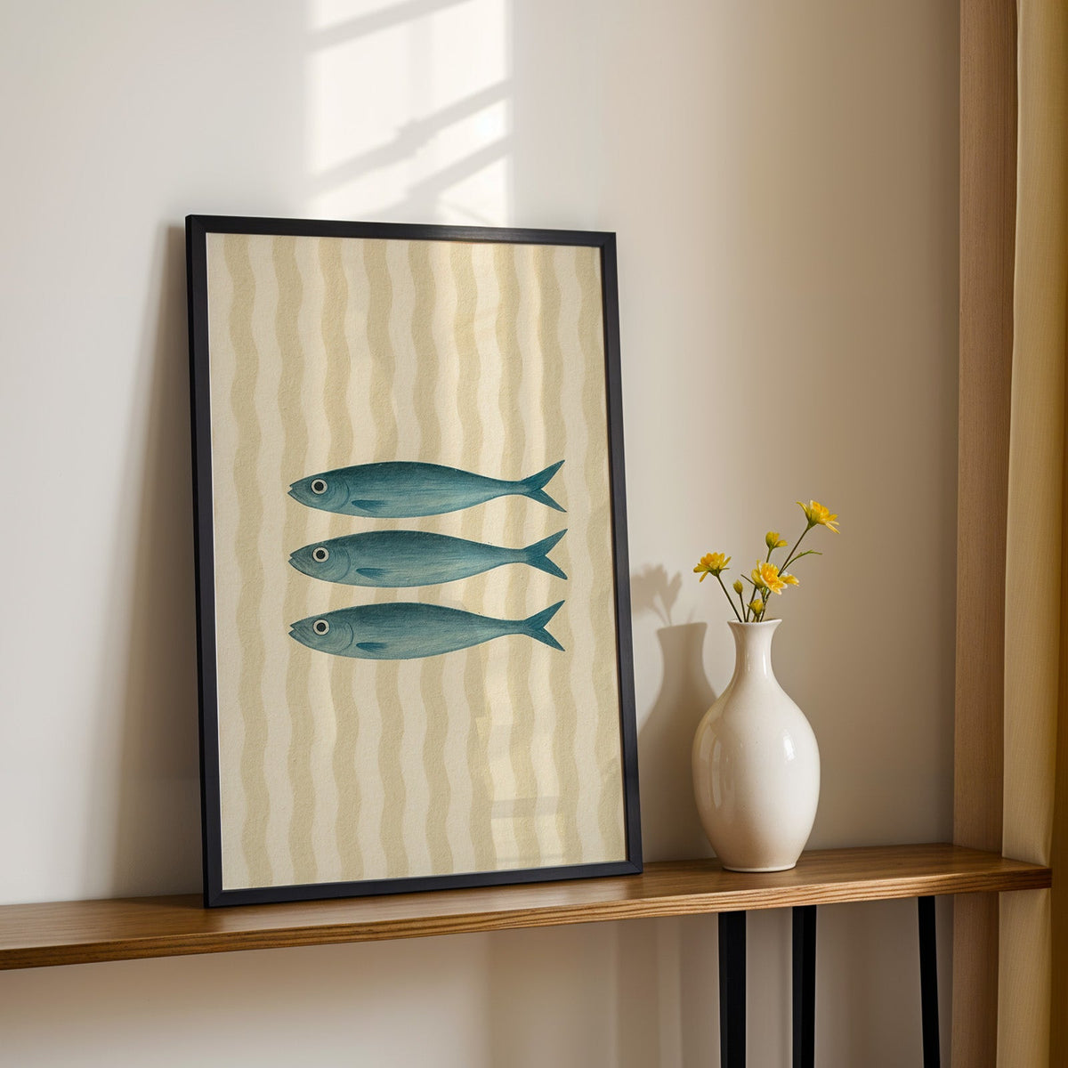 Three vintage sardines print in a black frame on a console table with daisies