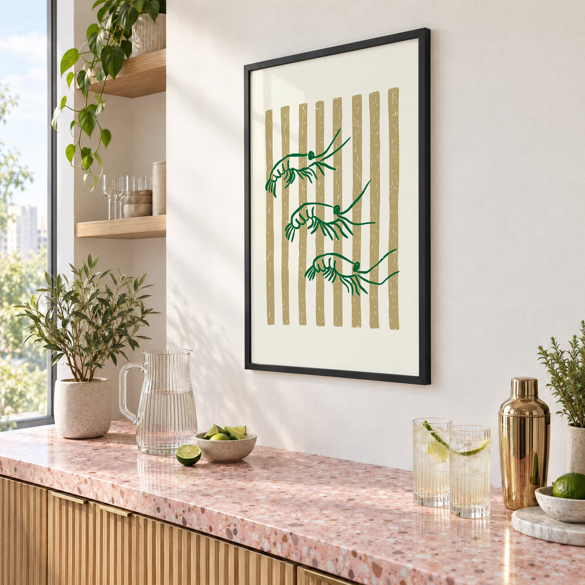 Three green shrimp on gold stripes print in a black frame above a pink terrazzo cocktail counter with limes, seen at an angle