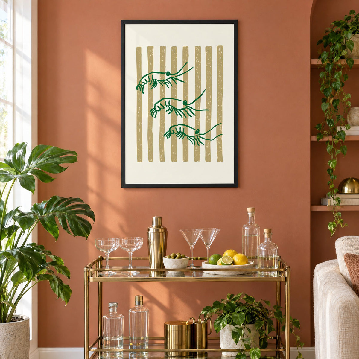 Three green shrimp on gold stripes print in a black frame on a terracotta wall above a brass bar cart with coupes and citrus