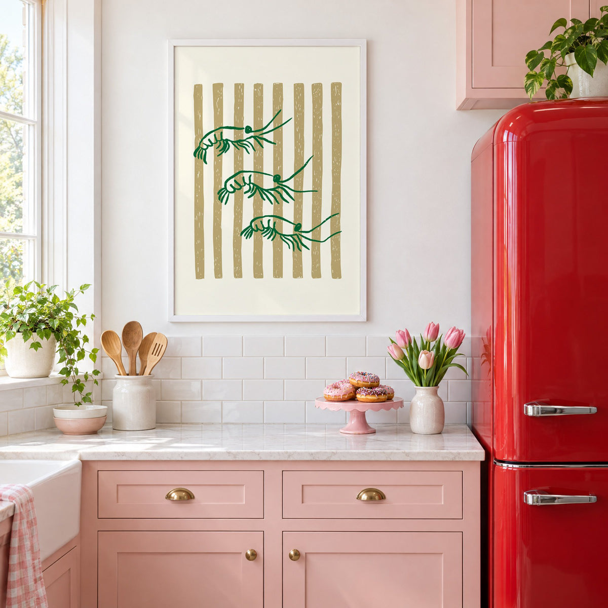Three green shrimp on gold stripes print in a white frame above pink cabinets beside a red retro fridge