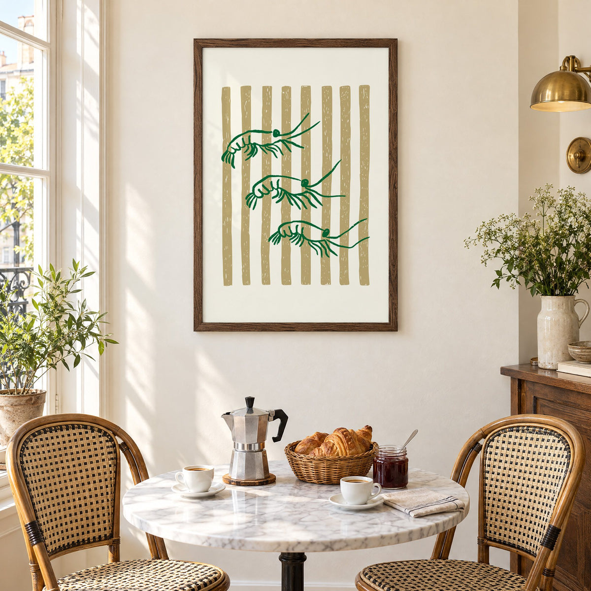 Three green shrimp on gold stripes print in a walnut frame above a marble bistro table with croissants and rattan chairs