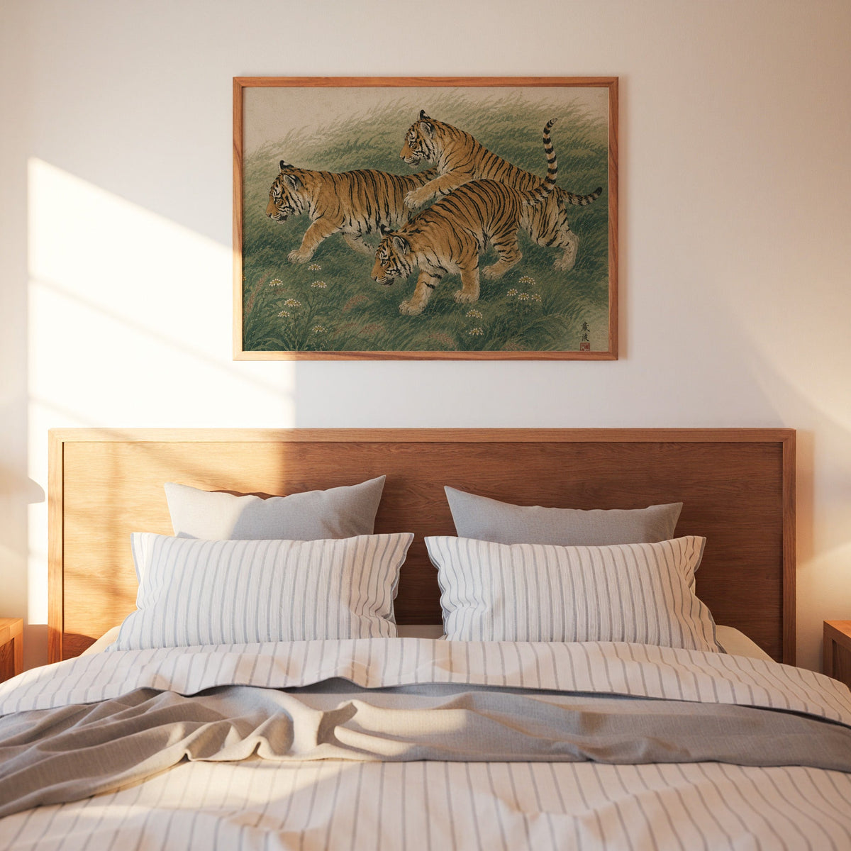 Three tiger cubs in tall grass print in a warm wood frame above a bed with striped linen bedding