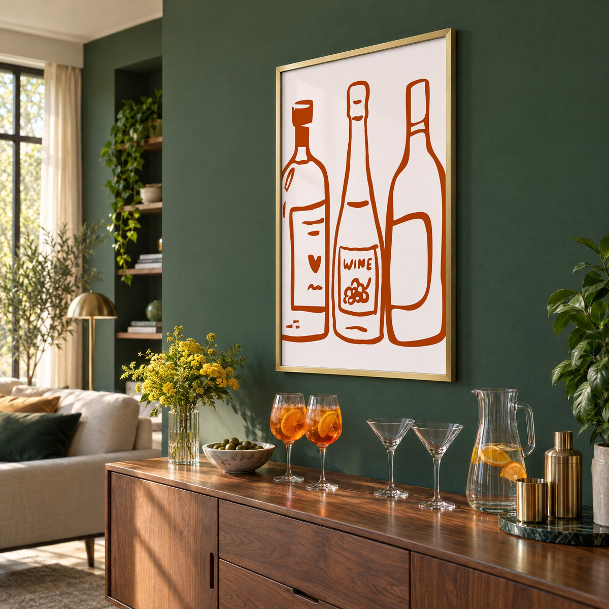 Three wine bottles rust brush line print in a brass frame on a bottle green wall above a sideboard with spritz and martini glasses, seen at an angle