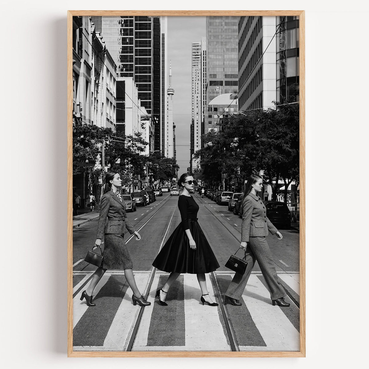 Three women crossing a city street print in a light oak frame on a plain white wall