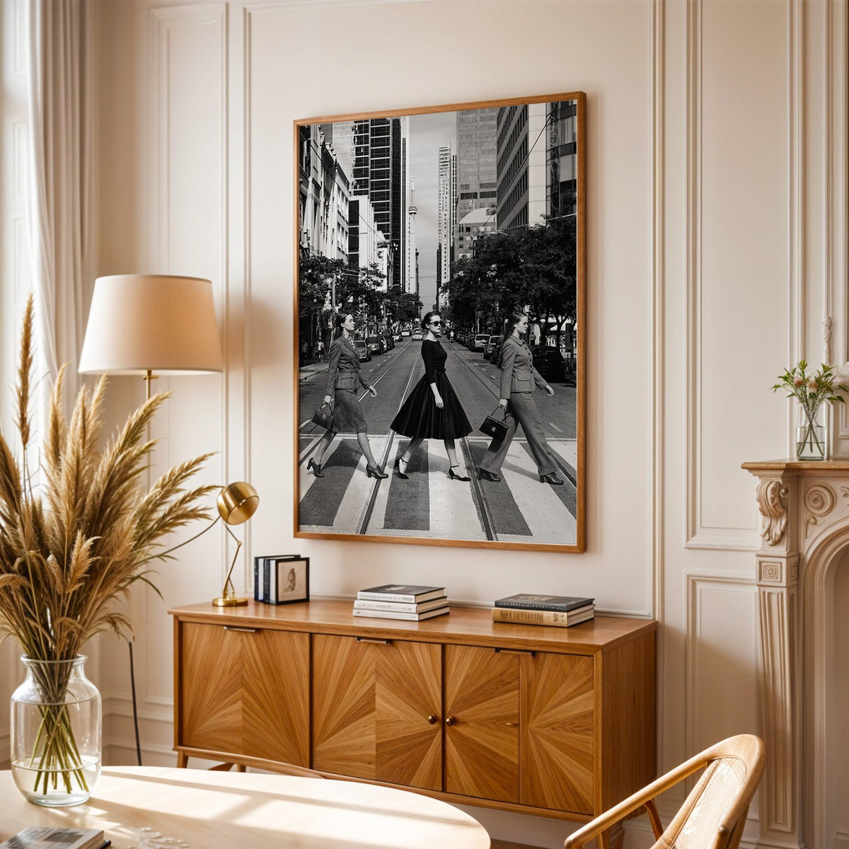 Three women crossing a city street print in an oak frame above a sunburst wood sideboard with pampas grass