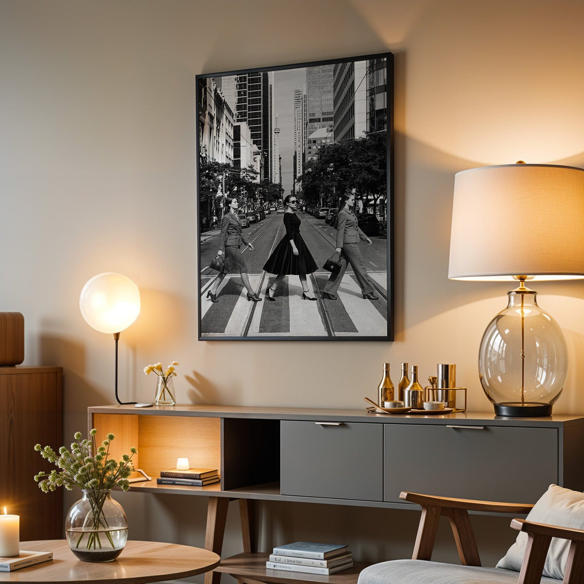 Three women crossing a city street print in a black frame above a grey media console with a glass table lamp