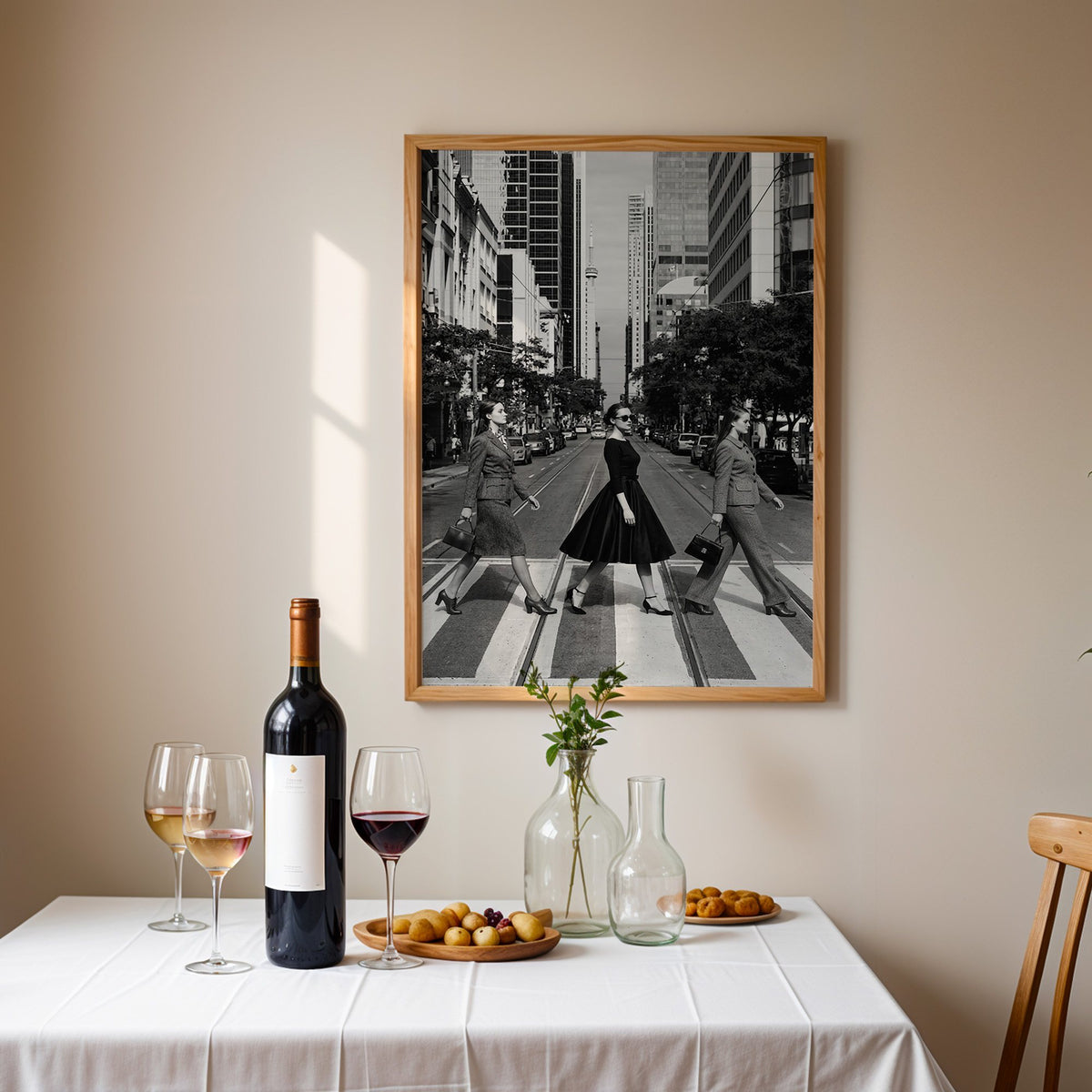 Three women crossing a city street print in an oak frame above a table set with red wine and glasses