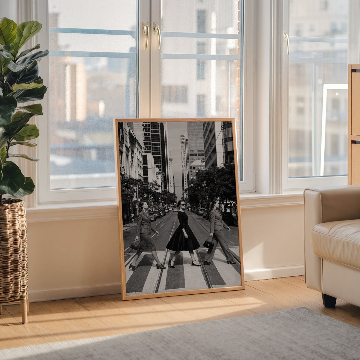 Three women crossing a city street print in an oak frame leaning on the floor beside a fiddle leaf fig