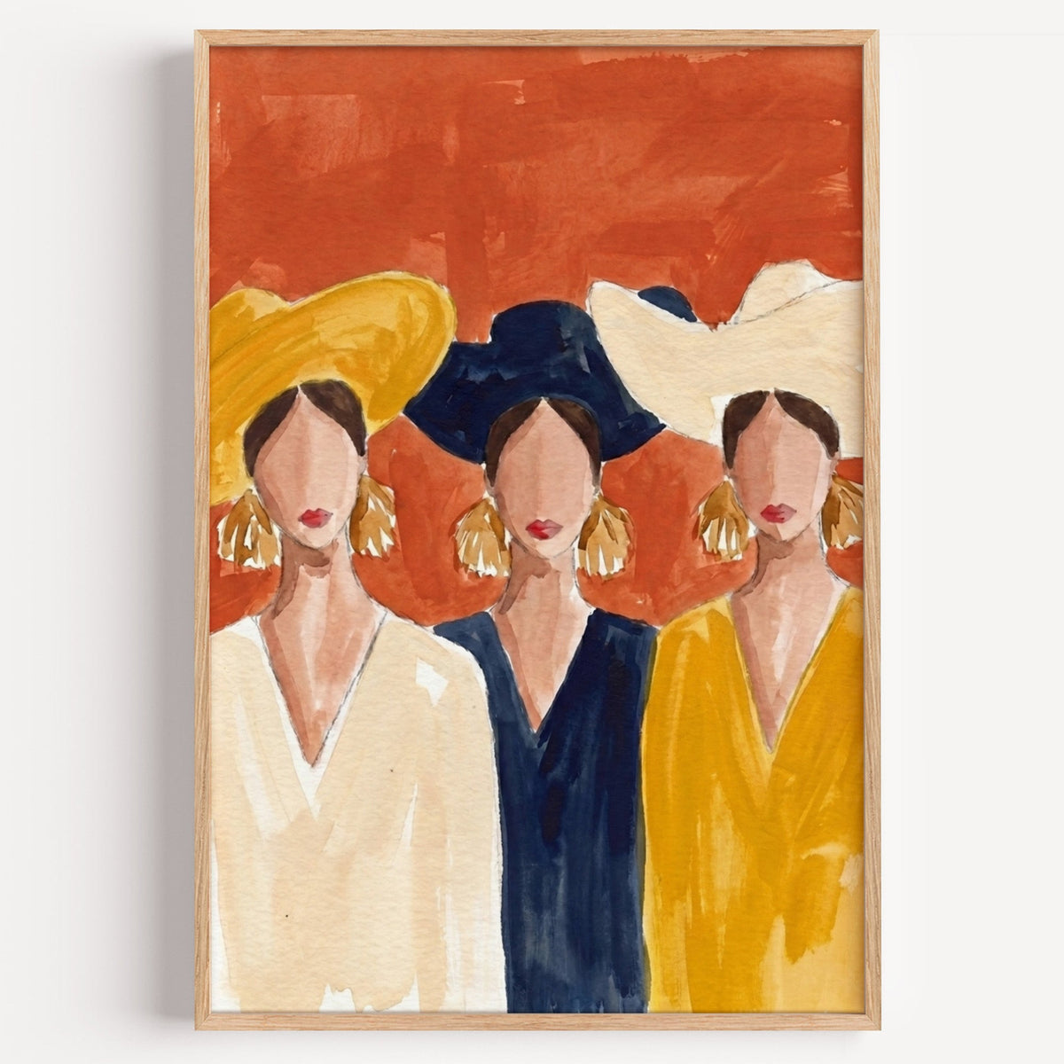 Three women in wide brim hats print in a light oak frame on a plain white wall