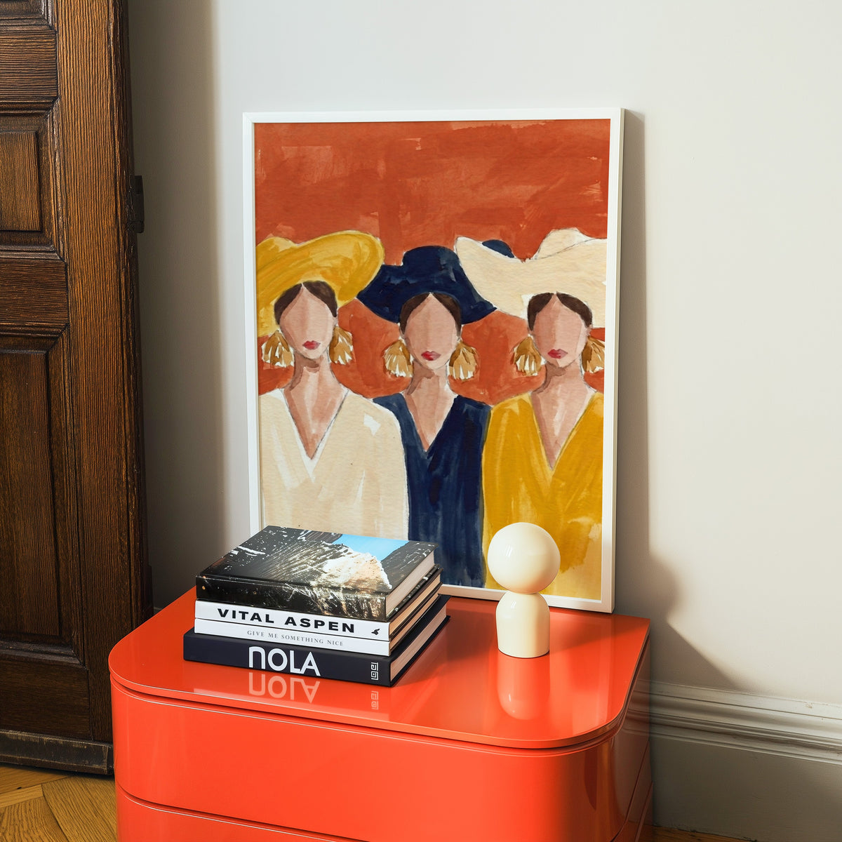 Watercolor fashion illustration print in a white frame on a glossy orange cabinet with books