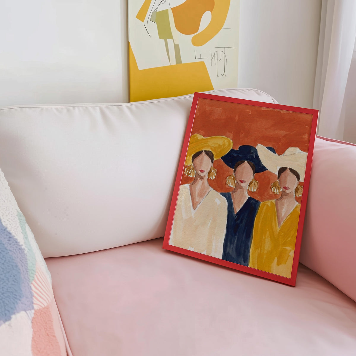 Women in hats print shown in a red frame leaning on a blush pink sofa
