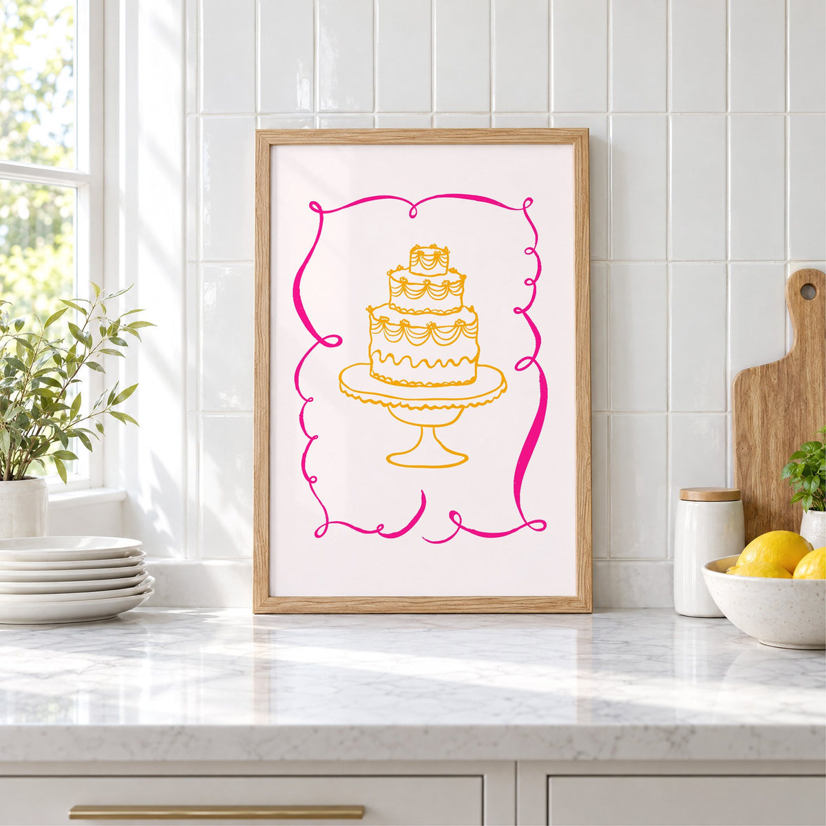 Tiered cake pink ribbon frame print in an oak frame leaning on a marble counter by white tiles and lemons