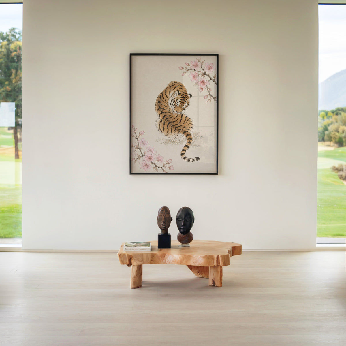 resting tiger with cherry blossom print in a black frame above a live-edge wood coffee table between garden windows