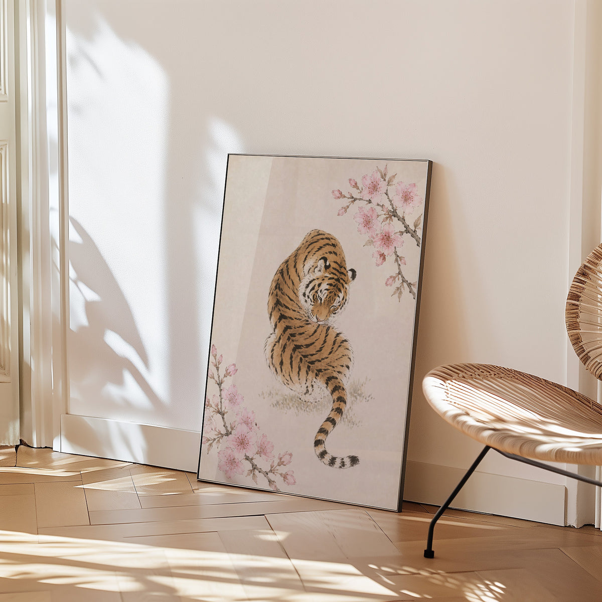 resting tiger with cherry blossom print in a black frame leaning on a herringbone floor beside a woven rattan chair