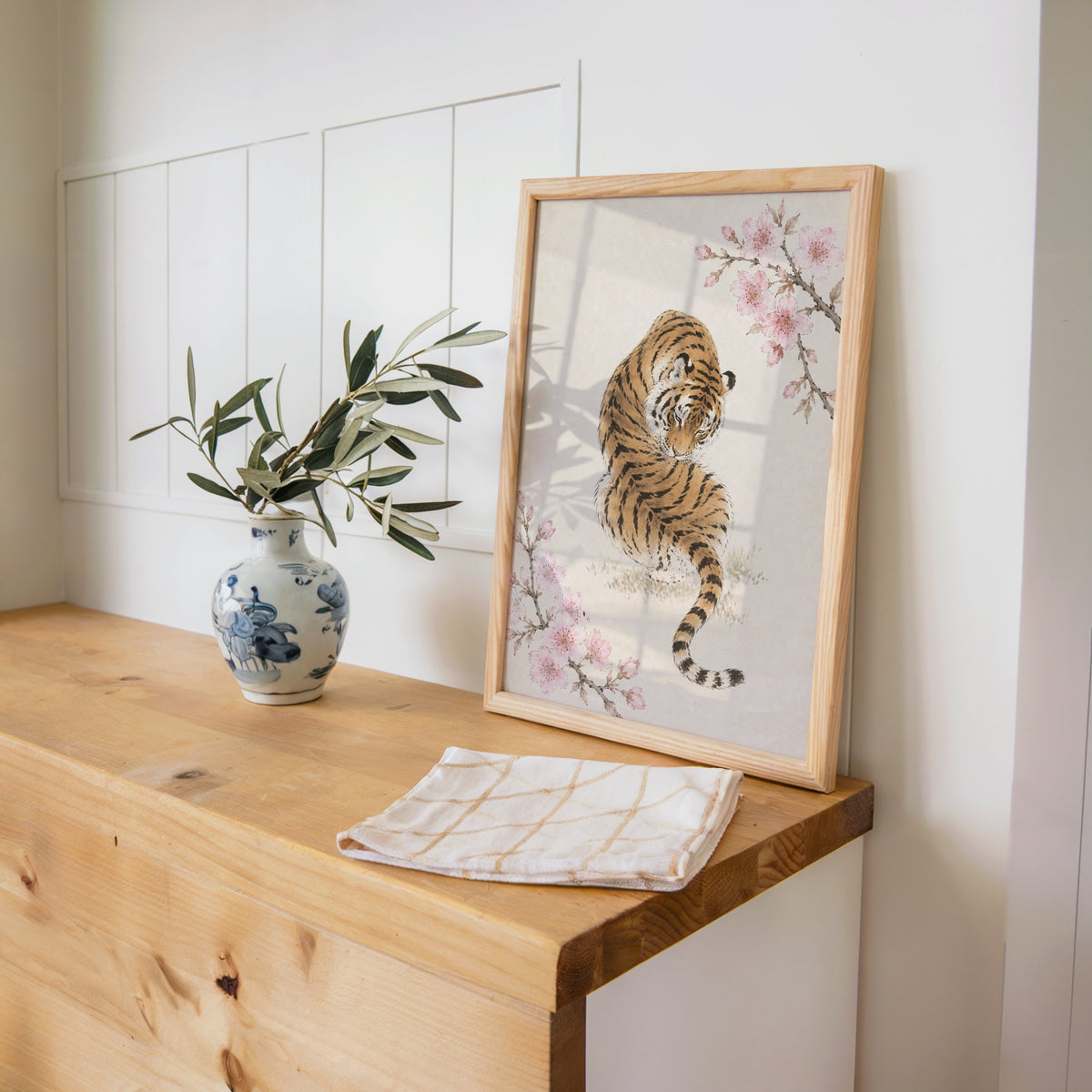 resting tiger with cherry blossom print in a pine frame on a wooden counter beside a blue and white porcelain vase