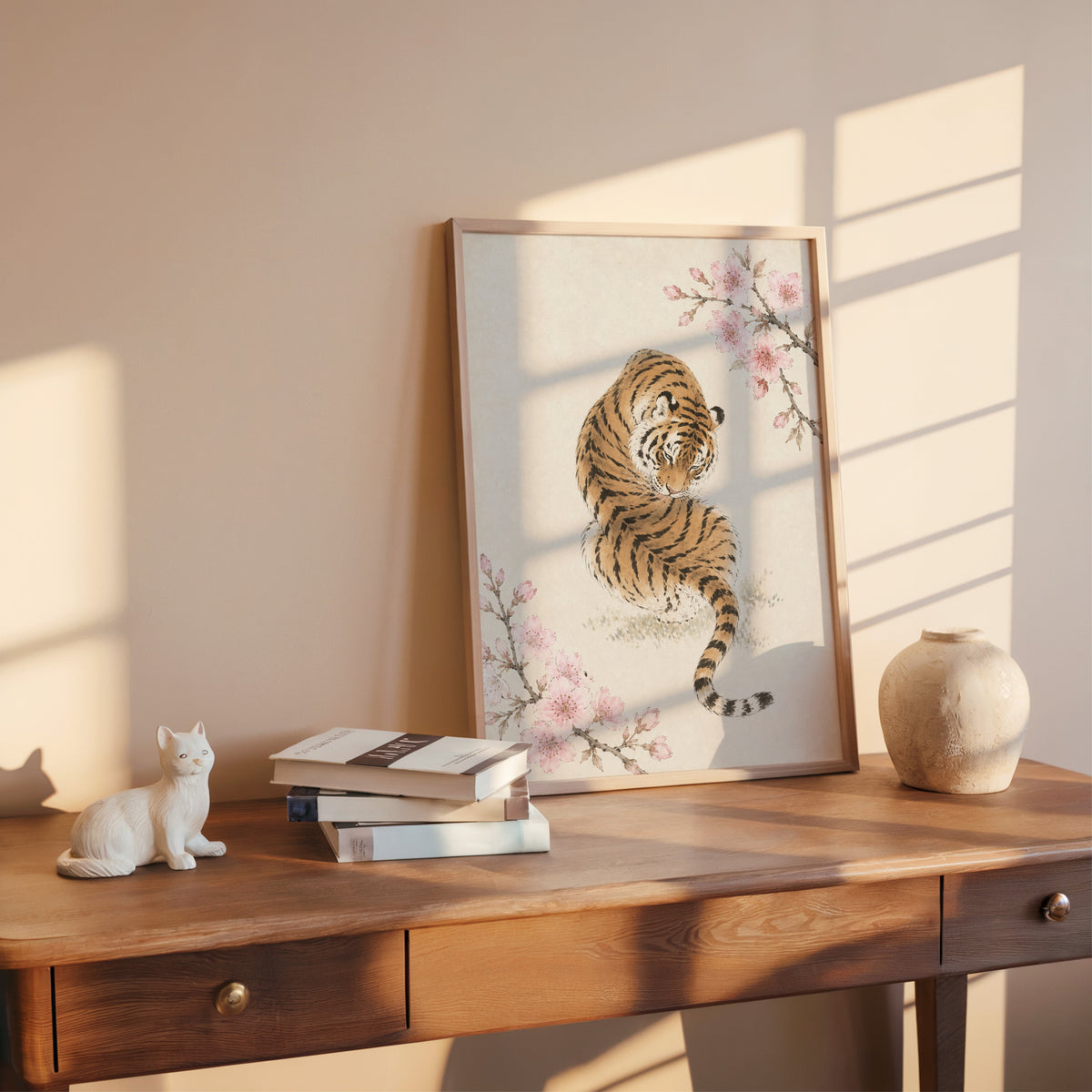 resting tiger with cherry blossom print shown in a rose gold frame leaning on a wooden writing desk with books