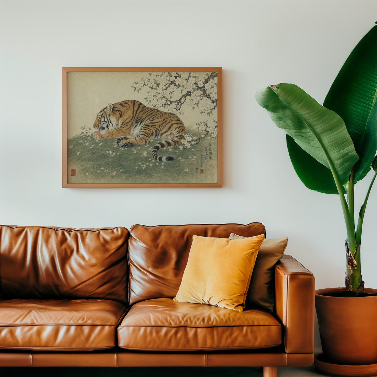 Tiger resting under cherry blossoms print in a warm oak frame above a cognac leather sofa with a mustard pillow
