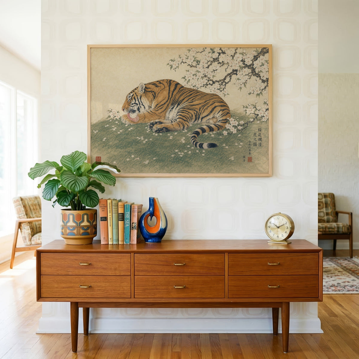 Tiger resting under cherry blossoms print in a light oak frame above a teak credenza with books and a brass clock