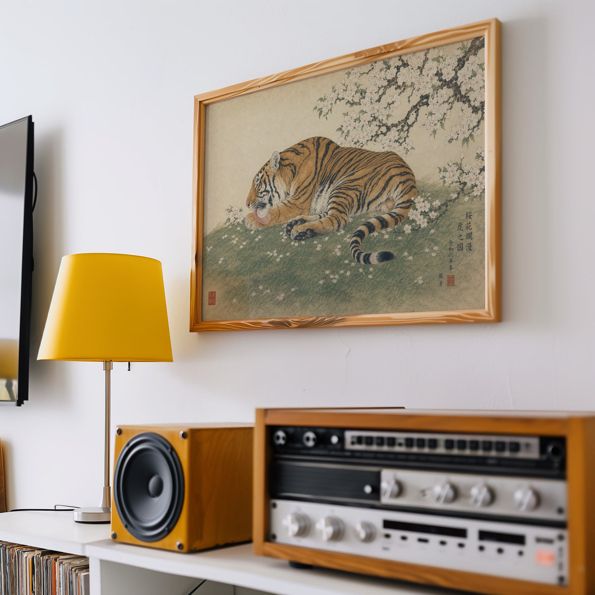 Tiger resting under cherry blossoms print in a pine frame above a vintage stereo and a yellow table lamp
